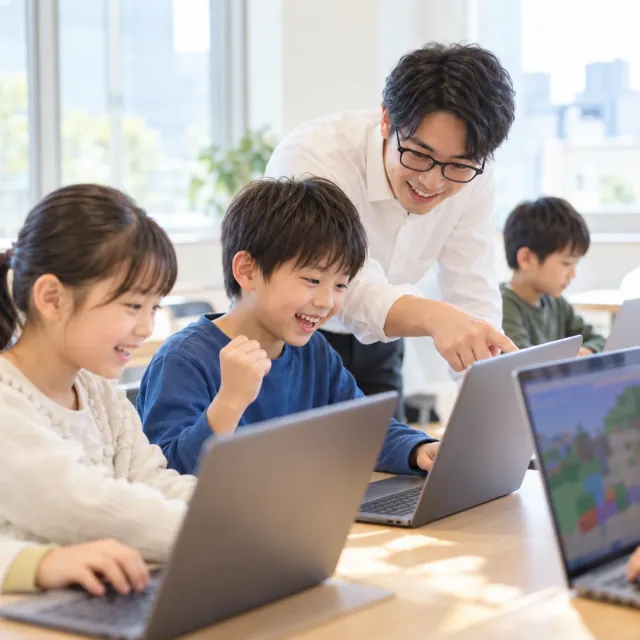 小学生がノートパソコンでプログラミングに取り組み、講師が横でサポートしている様子